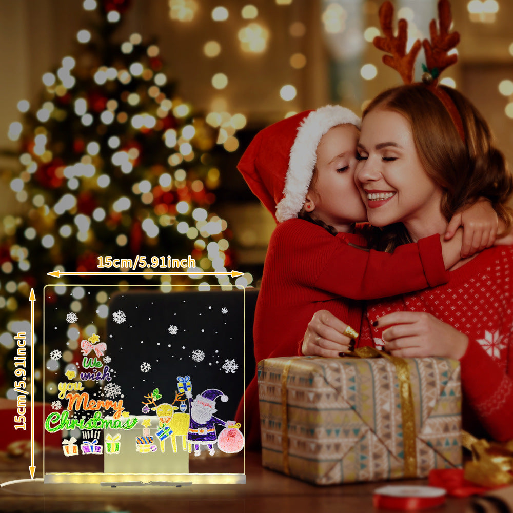 Woman and child in festive attire with a Christmas-themed light-up sign in front of a decorated tree.