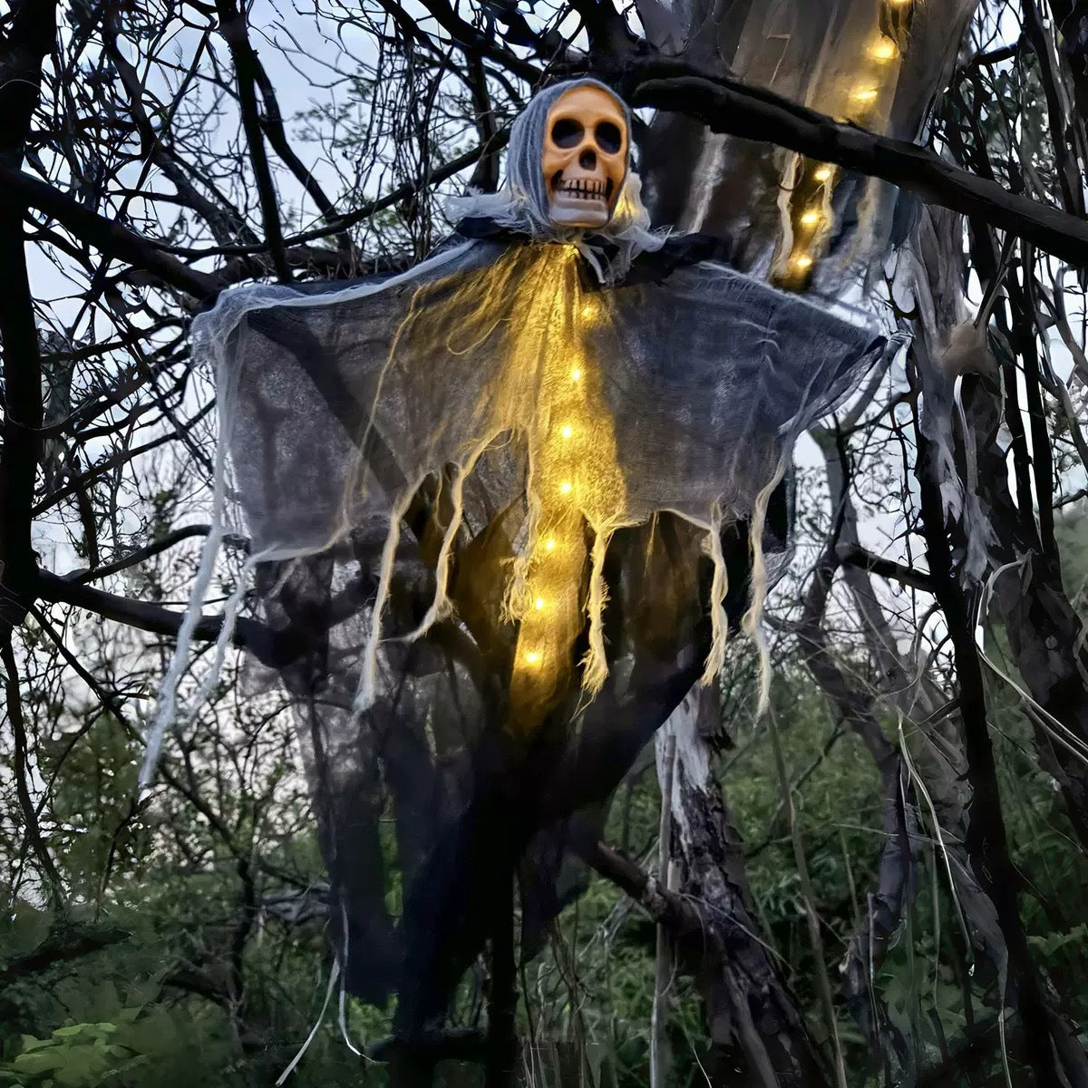 Halloween decoration of a ghostly figure with lights hanging from tree branches.