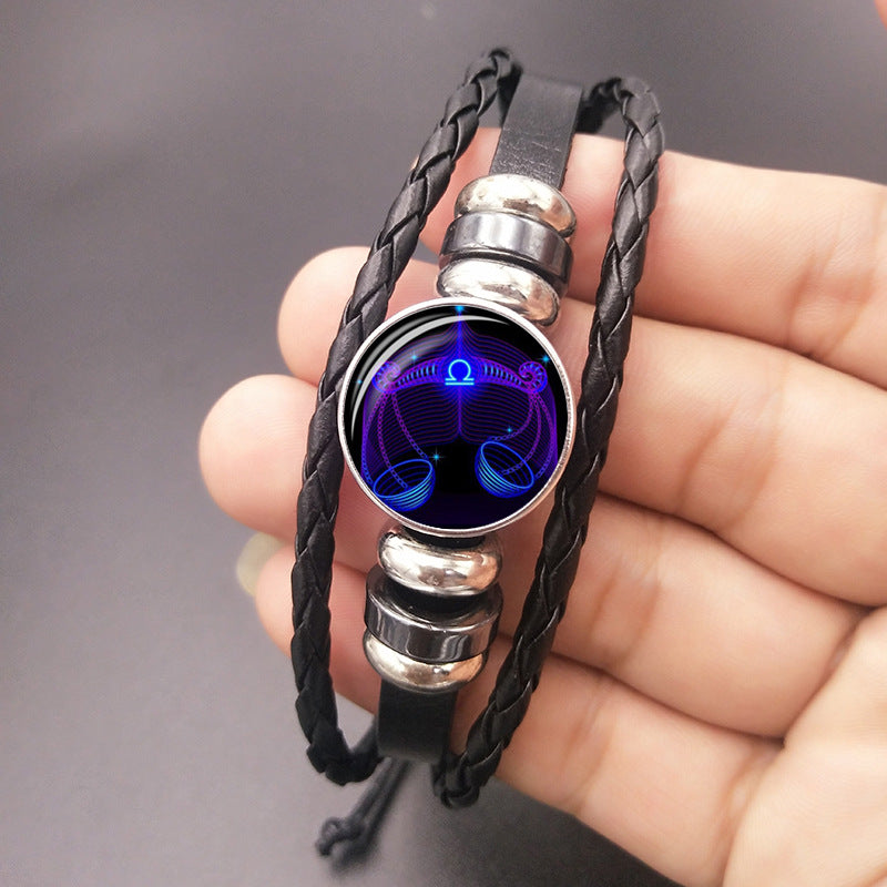 Black braided bracelet with a blue and purple circular pendant on a hand against a gray background