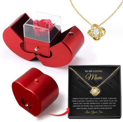 Red jewelry box with a rose, gold necklace, and black card for 'Mom' on a white background