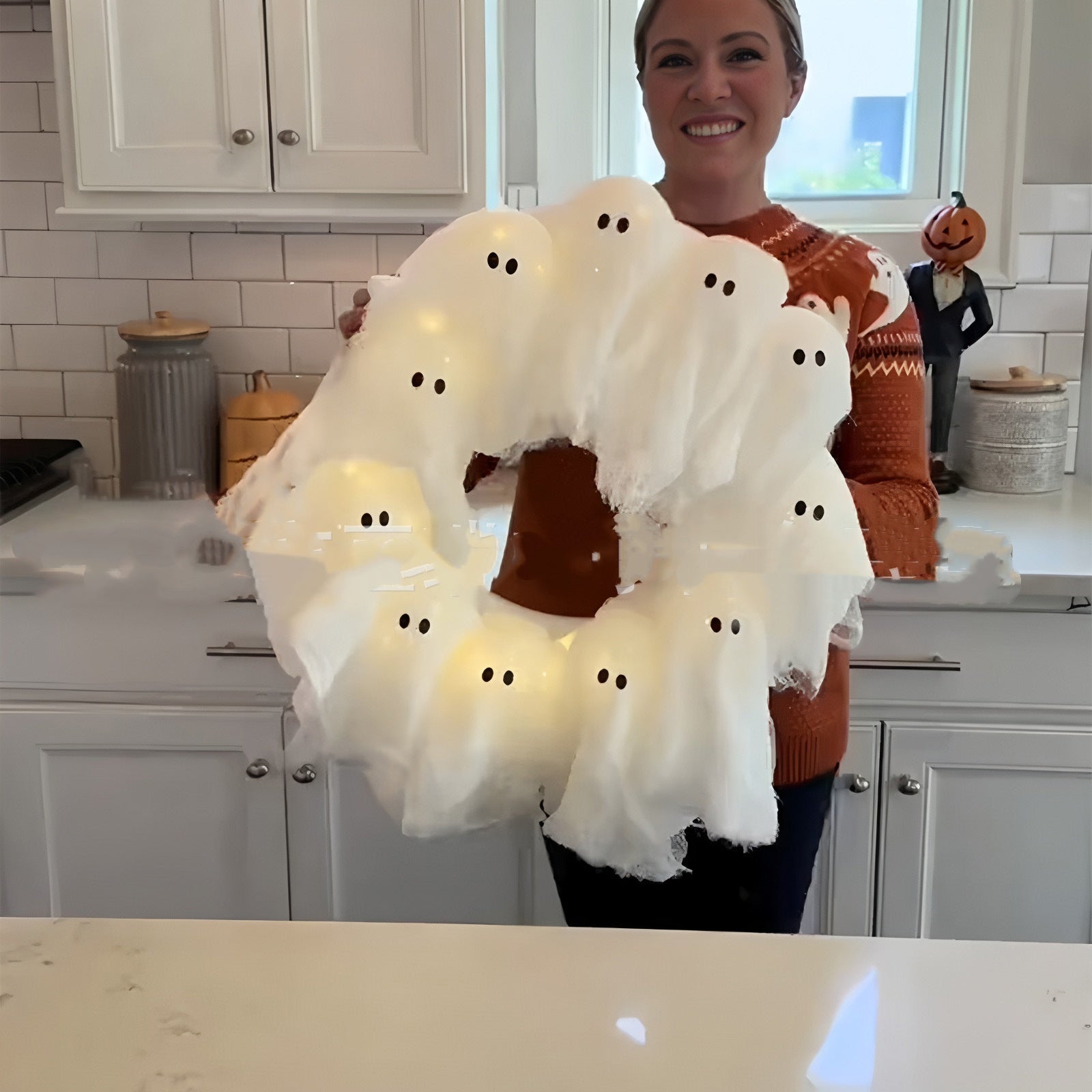 Person holding a Halloween wreath with ghost decorations in a kitchen.