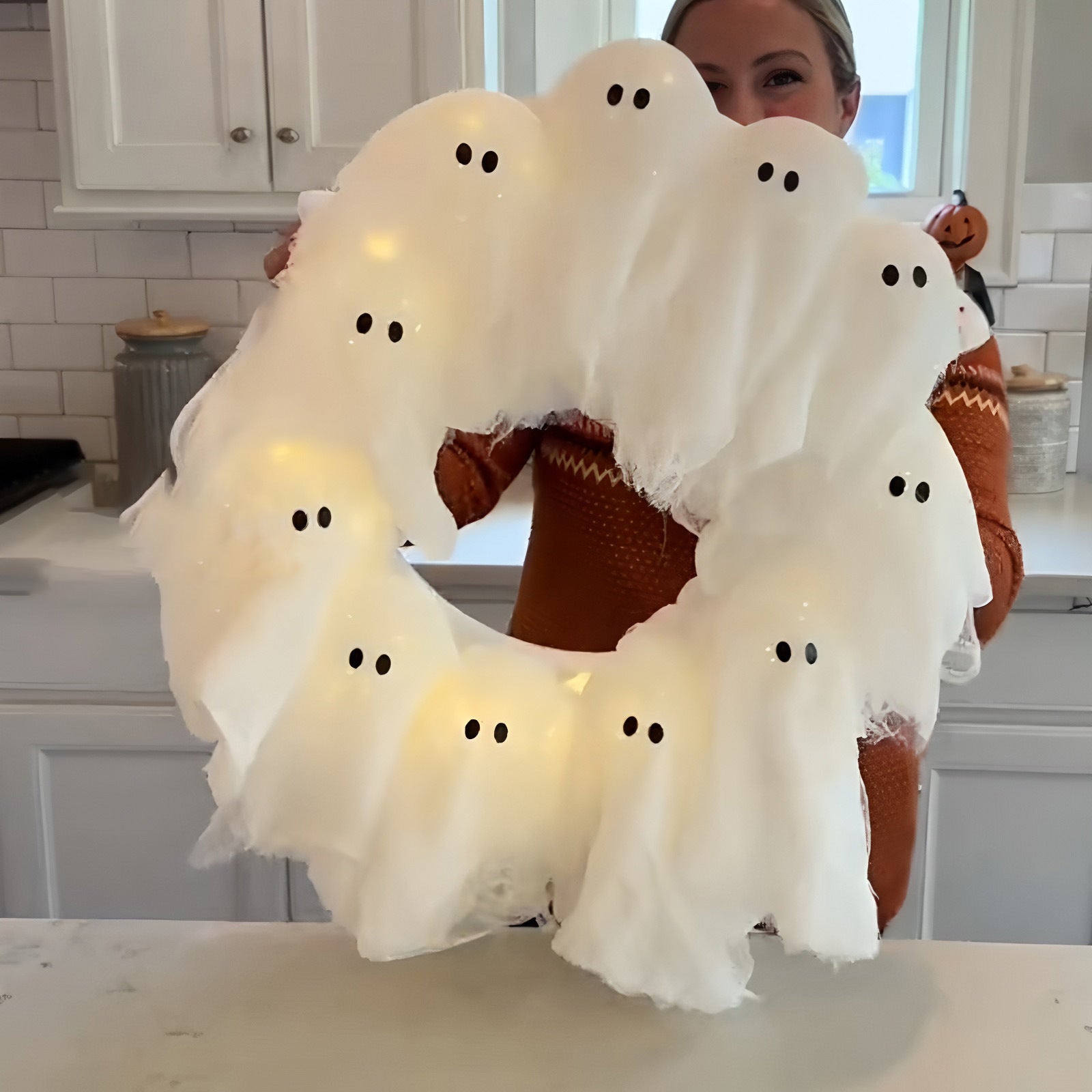 Person holding a Halloween wreath with ghost decorations in a kitchen.